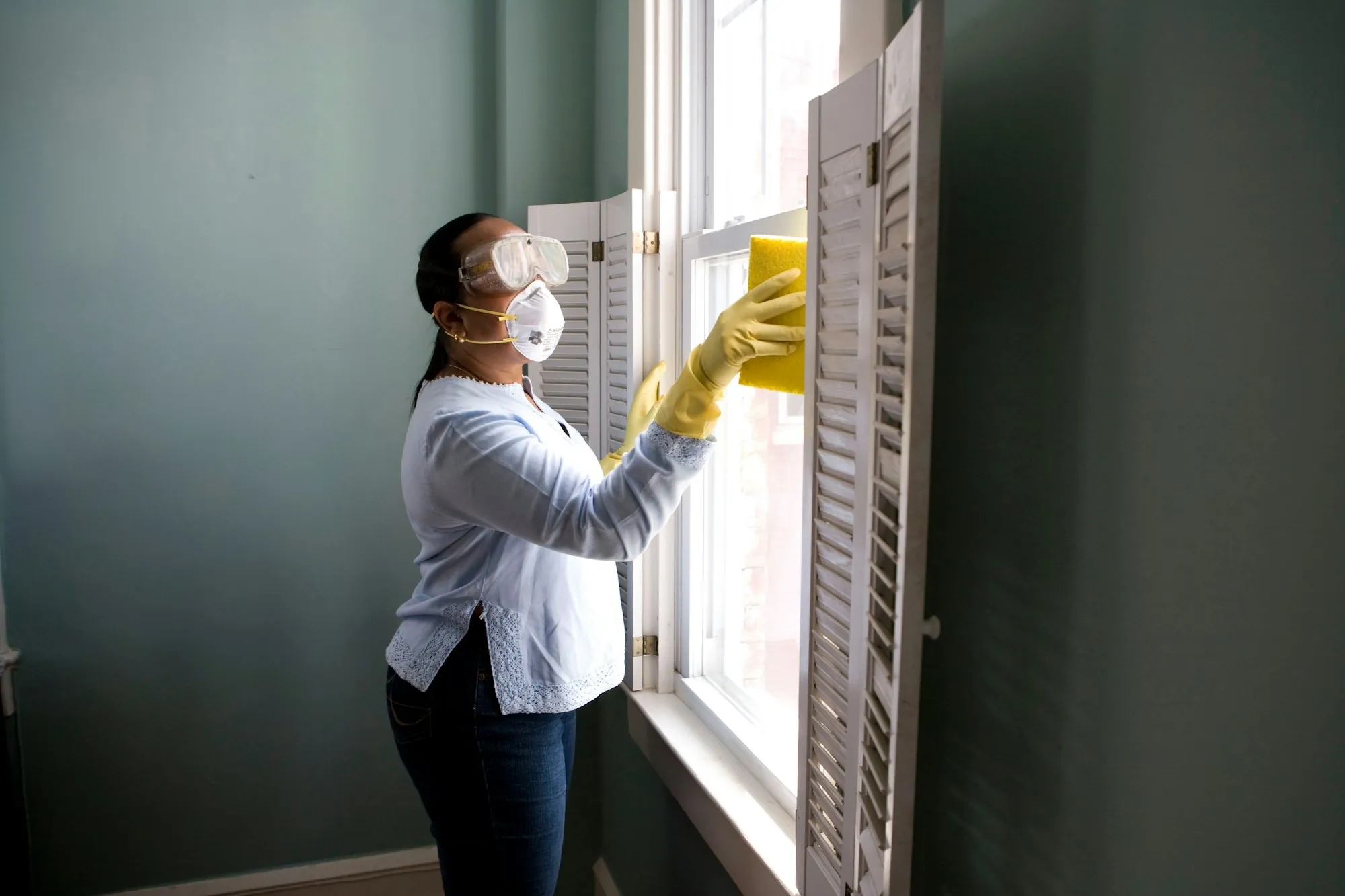 Cleaner in gloves and a mask wiping down a window frame