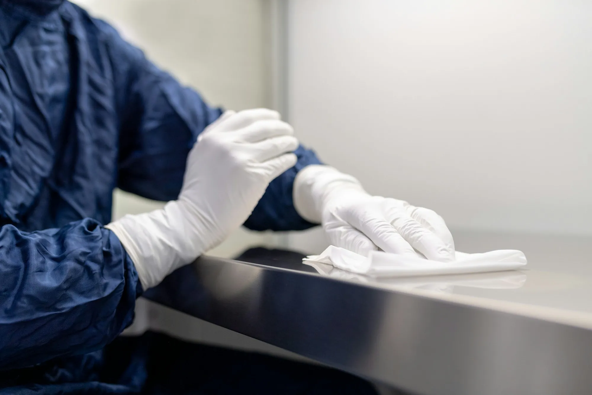 Worker in white gloves wiping down a steel counter