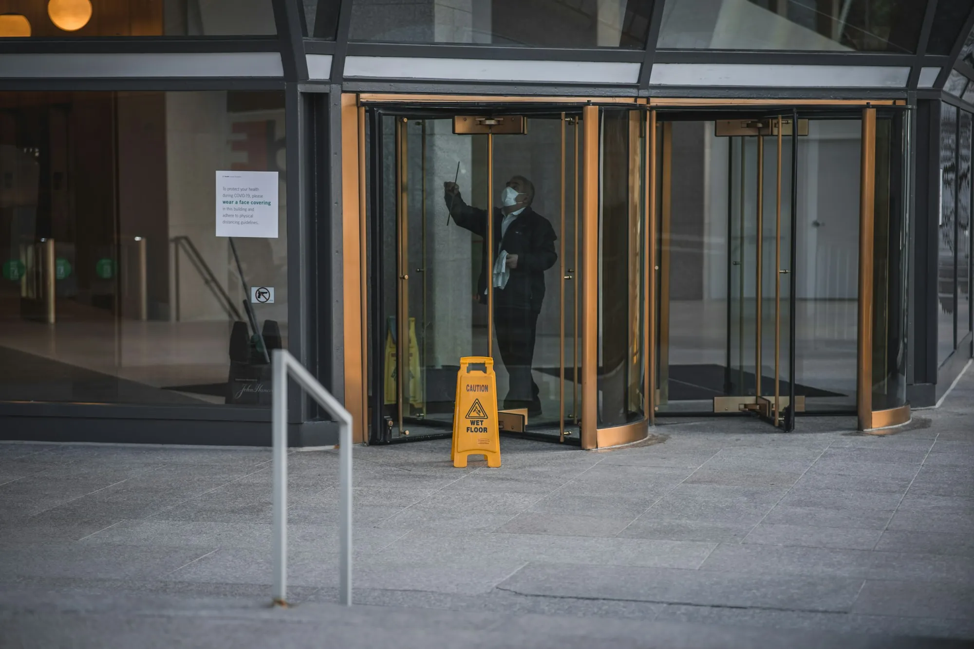 Cleaner wiping the glass of a revolving door beside a wet floor sign