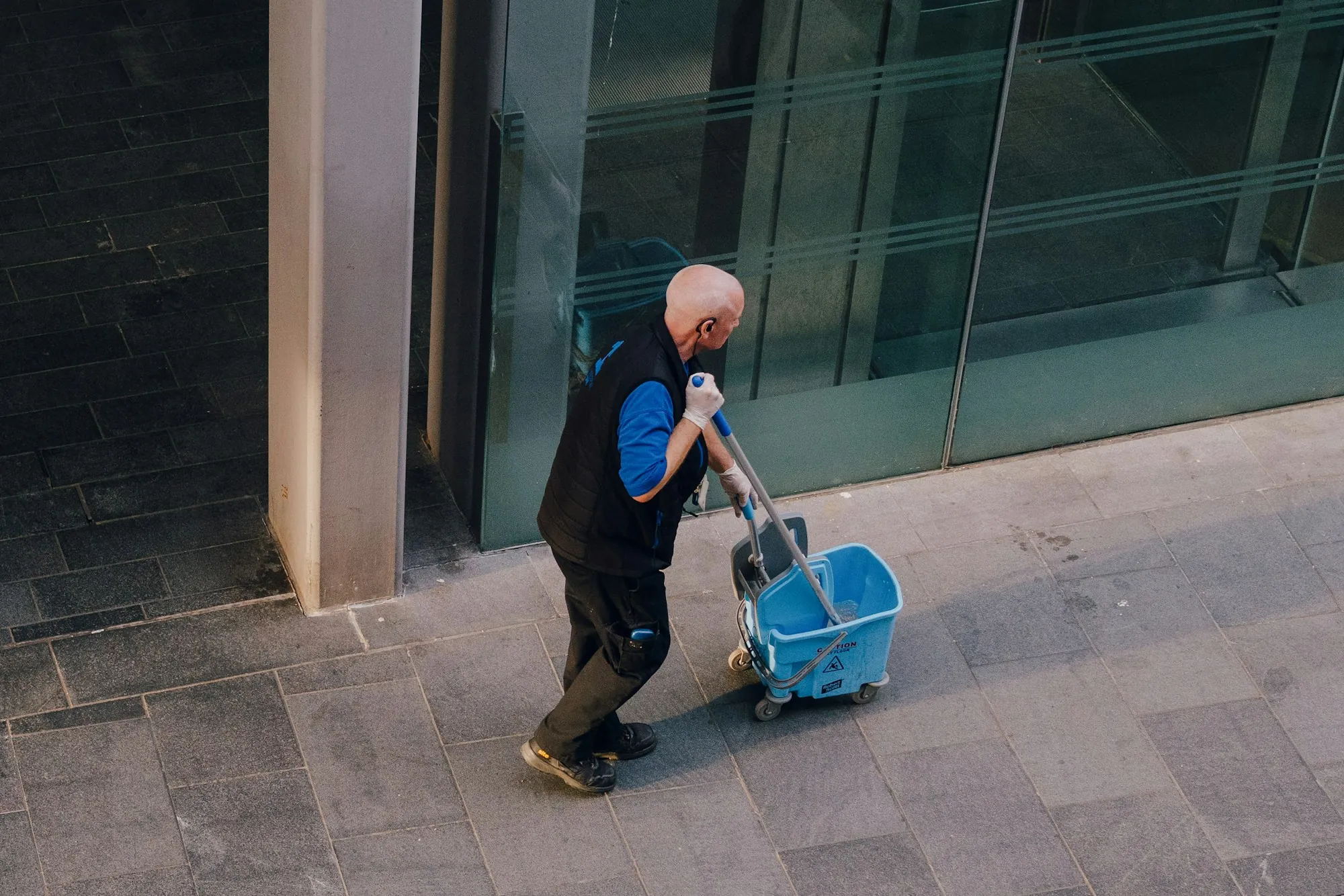 Cleaner pushing a mop bucket along a building entrance